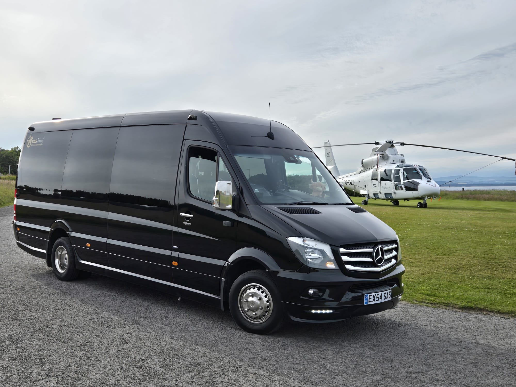 SAS Travel's black Mercedes-Benz Sprinter executive minibus parked beside a helicopter on the Scottish coast